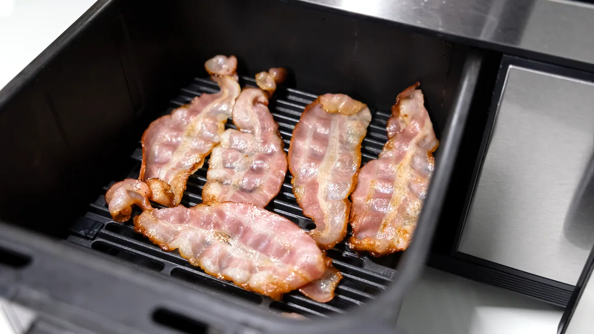 The open basket of an air fryer filled with glistening golden bacon.
