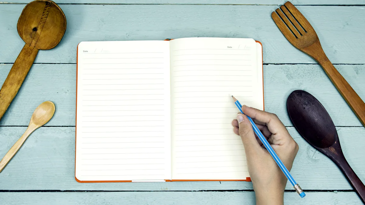 A blank recipe book lying open on a counter with a pencil resting beside it.
