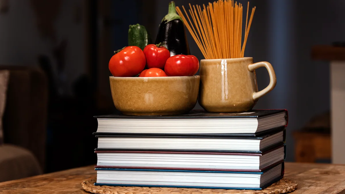 A neat stack of cookbooks on a wooden shelf, spines facing outward.