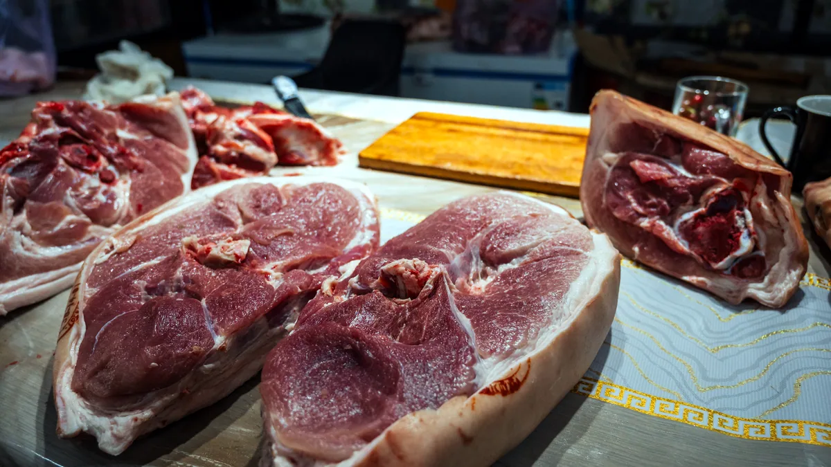 An assortment of raw meat cuts arranged on a butcher's steel counter.