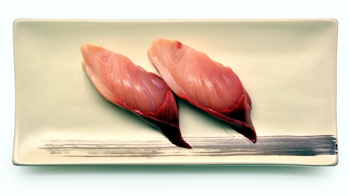 A raw duck breast with glossy skin laid on a dark wooden board.