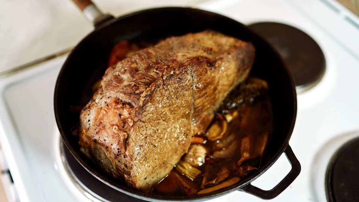 A large gammon joint browning in a deep roasting pan on the hob.