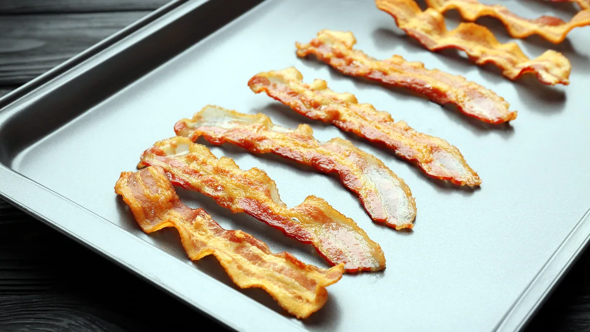 Crispy golden brown bacon strips laid flat on a wire rack over a tray.