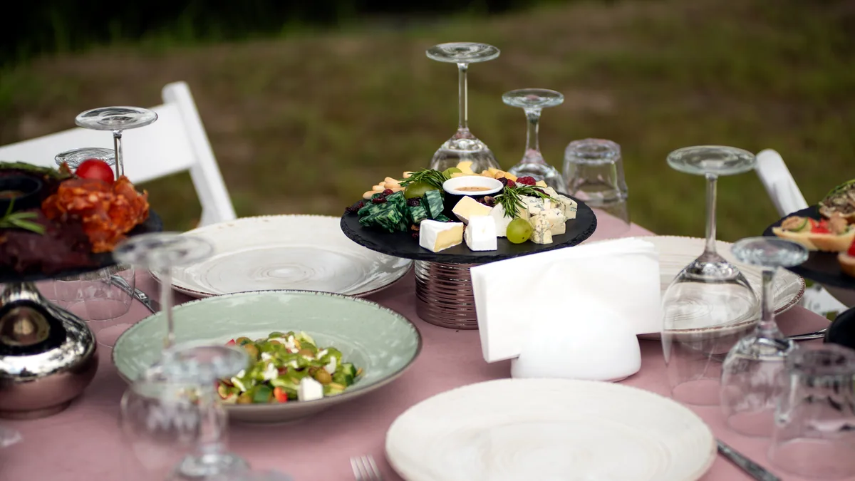 An elegant outdoor catering table dressed with linen, candles and game dishes.